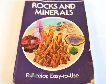 Może przedstawiać: Książka w stylu vintage zatytułowana "ROCKS AND MINERALS" z fioletową okładką. Okładka zawiera okrągłą ilustrację różnych skał i minerałów w odcieniach brązu, fioletu i zieleni. Tekst "Full-color, Easy-to-Use" jest wydrukowany na dole.