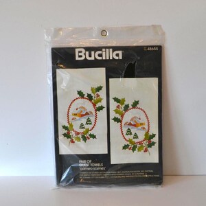 May include: A package of Bucilla embroidery kits for a pair of guest towels. The towels feature a winter scene with a red house, green trees, and holly.