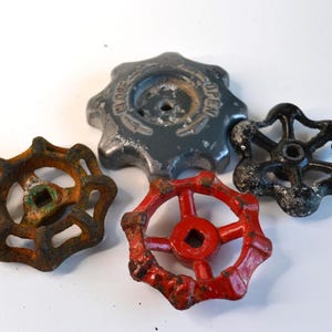 May include: Four vintage valve handles in various colors and conditions. The handles include a rusty brown, a bright red, a black, and a gray handle. The gray handle has the word "OPEN" on it.
