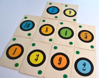 May include: A set of vintage playing cards numbered 1 to 10. Each card has a number within a coloured circle, including orange, yellow, green, and blue, with a black border. Green dots are in each corner of the cards.