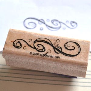 May include: A wooden stamp with a decorative swirl design and the text "© 2007 STAMPIN' UP!". The stamp has a rectangular shape and is made of light-colored wood. A stamped impression of the design is visible on a white paper.