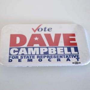 May include: A rectangular campaign button with rounded corners. The button features the words "Vote DAVE CAMPBELL" in red and blue, with "FOR STATE REPRESENTATIVE DEMOCRAT" below. A red checkmark is above the word "Vote".