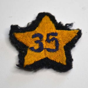 May include: Embroidered star-shaped patch with a yellow center and black border. The number "35" is stitched in blue across the center. This vintage patch could be used for clothing or crafts.