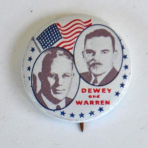 May include: A vintage campaign button featuring portraits of two men, with an American flag and the words "DEWEY and WARREN." The button is white with blue stars and a pin on the back.
