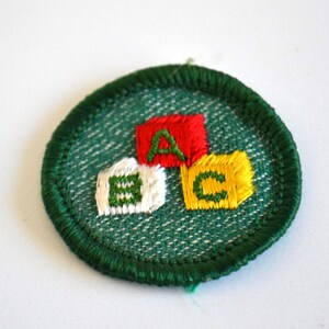 May include: Embroidered patch featuring the letters "A", "B", and "C" on colorful blocks. The patch has a green border and a textured green background. The letters are in red, white, and yellow.