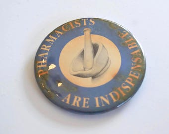 May include: A circular badge with the text "PHARMACISTS ARE INDISPENSABLE" around the edge. The badge features a mortar and pestle illustration in the centre, set against a blue and gold background.