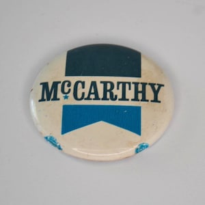 May include: A white button with blue and green stripes and the text "MCCARTHY" in black letters.