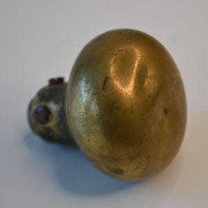 May include: A brass door knob with a rounded, bulbous shape. The knob has a worn, aged patina and is slightly tarnished.