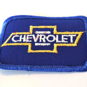 May include: A blue embroidered patch featuring the Chevrolet logo in yellow and white. The patch has a blue border and the word "CHEVROLET" is stitched across the center.