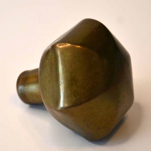 May include: A brass door knob with a geometric, faceted design. The knob is a dark gold color and has a smooth, polished finish.