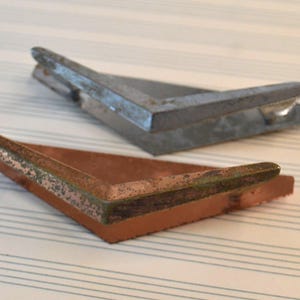 Puede incluir: Dos soportes de esquina metálicos, uno es plateado y el otro es cobre. Ambos tienen un aspecto desgastado y envejecido.