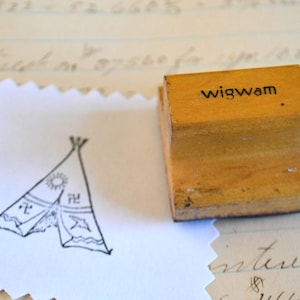 May include: A wooden stamp with the word "wigwam" printed on top. A stamped image of a wigwam with a sun and other symbols is on a white, scalloped-edge paper. The background is a vintage paper with handwritten text.