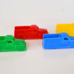 Könnte beinhalten: Vier bunte Spielzeug-Pick-up-Trucks in Grün, Rot, Blau und Gelb sind auf einer weißen Oberfläche angeordnet. Die Trucks haben ein klassisches Design mit Kabine und Ladefläche.