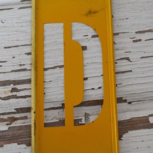 Plantilla de latón industrial pintada de amarillo vintage: letra mayúscula D del alfabeto