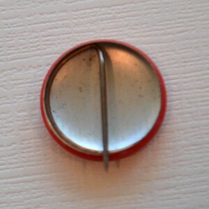 May include: The back of a red button with a silver pin attached.