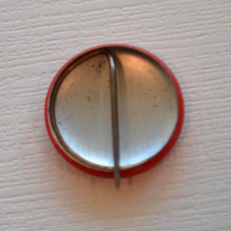 May include: The back of a red button with a silver pin attached.
