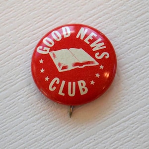 May include: Red and white enamel pin with the words "GOOD NEWS CLUB" and an image of an open book.