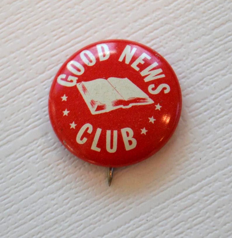 May include: Red and white enamel pin with the words "GOOD NEWS CLUB" and an image of an open book.