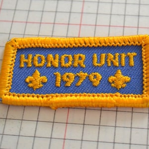 May include: Embroidered patch with the words "HONOR UNIT 1979" in gold thread on a blue background. The patch has a gold border and two gold fleur-de-lis symbols.