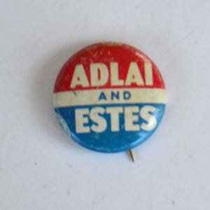May include: A vintage campaign button with a red top section, a white middle section, and a blue bottom section. The button reads "ADLAI" in white letters on the red section and "AND" in black letters on the white section. The bottom section reads "ESTES" in white letters.
