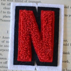 May include: Red felt letter N with a black border. The letter is on a white background.
