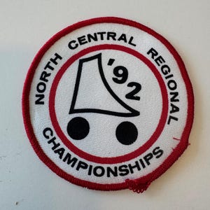 May include: A white, red, and black circular patch with the text "North Central Regional Championships '92". A black and white illustration of a roller skate is in the center of the patch.