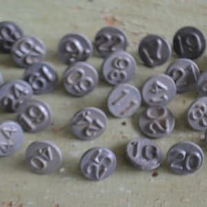 May include: A collection of 30 round metal tags with numbers printed on them. The tags are silver in color and have a slightly worn appearance.