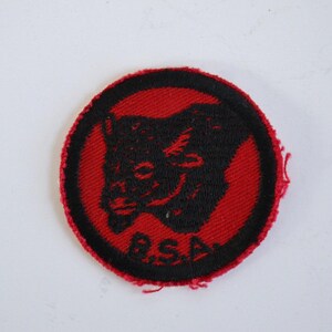 May include: A red and black embroidered patch with a black wolf head and the letters "R.S.A." in black.
