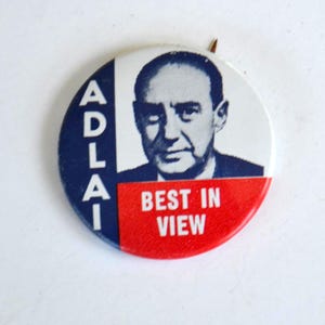May include: A vintage campaign button featuring a portrait of a man. The button has a white background with the man's image and the text "ADLAI" in blue. The bottom section is red with the words "BEST IN VIEW".