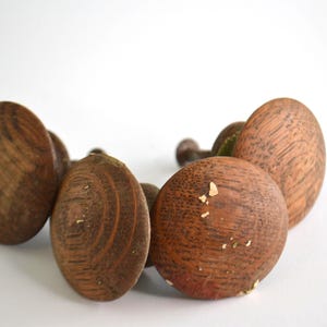 Puede incluir: Un conjunto de cuatro pomos redondos de madera con un patrón de veta natural visible. Cada pomo presenta una superficie lisa y abovedada en un tono marrón medio, con pequeñas motas claras dispersas por la textura de la madera frontal.