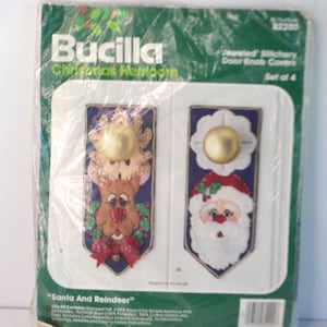 May include: A Bucilla Christmas Heirloom kit for Jeweled Stichery Door Knob Covers. The package contains a set of four covers with Santa and reindeer designs. The covers feature gold-colored knobs and colorful felt applique details.