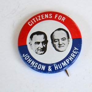 May include: A vintage political campaign button with a red and blue border. The button features portraits of two men and the text "CITIZENS FOR JOHNSON & HUMPHREY" in white lettering. A pin is attached to the back.