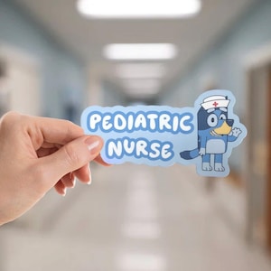 May include: A light blue sticker with the words "PEDIATRIC NURSE" in white, featuring a cartoon dog character wearing a nurse's hat. The sticker is held in front of a blurred hospital hallway.