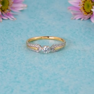 Op de afbeelding: Een gouden ring met een centrale briljant geslepen diamant, geflankeerd door twee taps toelopende secties bezet met kleine pavé-diamanten. De ringband is vervaardigd van gepolijst geelgoud, wat dit sieraad een strakke en verfijnde uitstraling geeft.