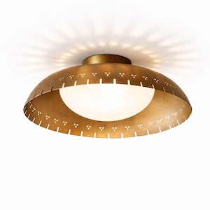 May include: A gold-coloured, dome-shaped ceiling light fitting with a white, spherical light source. The fitting has decorative cut-out patterns around the edge and is mounted on a white ceiling. The light casts a pattern on the ceiling.
