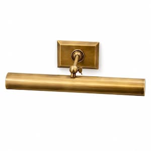 May include: A wall-mounted picture light with a brushed brass finish. The fixture features a rectangular backplate, a single adjustable arm with a swivel joint, and a long, cylindrical horizontal light housing for illuminating artwork.