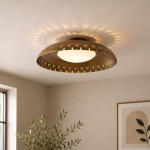 Puede incluir: Una lámpara de techo en forma de cúpula con acabado en bronce metálico. La pantalla presenta un borde perforado con pequeños recortes triangulares que rodean un globo central de vidrio blanco esmerilado que emite una luz cálida.