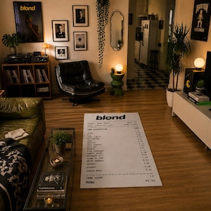 May include: A rectangular area rug featuring a white background with black text designed to look like a long receipt. The text includes the word blond at the top, a list of song titles, and a total at the bottom. The rug is placed on a wooden floor.
