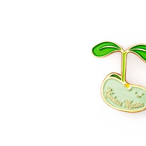 Pu&ograve; includere: Uno spillo in smalto verde a forma di germoglio di fagiolo con le parole "Kindness Matters" scritte su di esso.