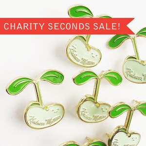 May include: Six gold-tone enamel pins with a green sprout and a white bean with the text "Kindness Matters" in gold lettering.