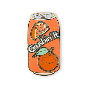May include: Orange soda can enamel pin with the text "Crushin' It" in white letters with a green leaf and orange slice.