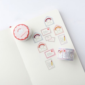 May include: Two rolls of washi tape with a rainbow and envelope design. The tape is pink, blue, and white with a red heart and a cute face on the envelope. The tape is on a white surface with several stickers of the same design.