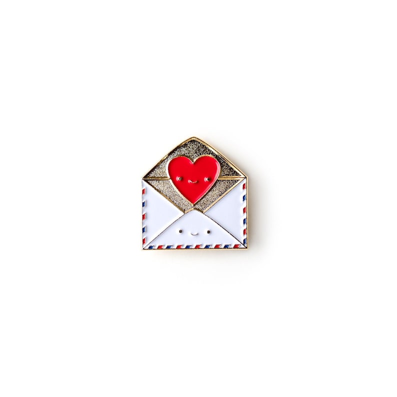 May include: Gold-tone enamel pin featuring a red heart with a smiling face inside a white envelope with a blue and red border.