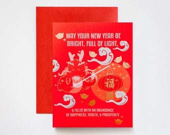 May include: Red and gold Chinese New Year greeting card with a cartoon dragon holding a lantern that says "福" (fu) which means good fortune. The card reads "May your new year be bright, full of light, & filled with an abundance of happiness, health, & prosperity."