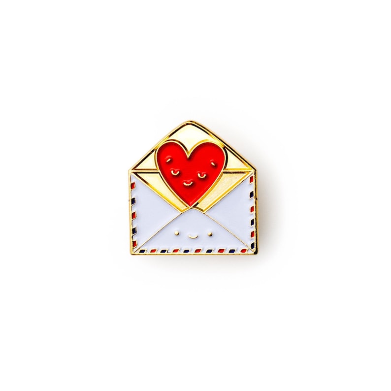 May include: Gold-tone enamel pin featuring a red heart with a smiling face inside a white envelope with a smiling face. The envelope has a blue and red striped border.