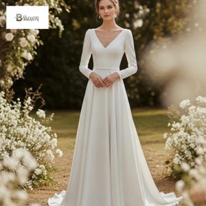 Puede incluir: Vestido de novia blanco con mangas largas y cuello en V. El vestido tiene un corpiño ajustado y una falda fluida. La modelo está de pie en un jardín con flores blancas en el fondo. El vestido tiene un diseño simple y elegante.