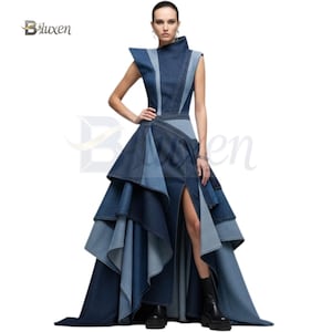 Peut inclure: Robe sans manches en jean de différentes nuances de bleu. La robe présente un col montant, des épaules structurées et une jupe à volants avec une fente haute sur la cuisse. La robe a une longue traîne et est portée avec des bottes noires.