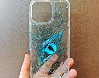 May include: Clear phone case with a blue eye design. The case has a textured, watery appearance with a large, detailed blue eye in the center. The eye has a black pupil and is surrounded by blue accents.