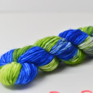 May include: A skein of colorful yarn in shades of blue and green. The yarn is tightly wound, with sections of bright blue, light blue, and vibrant green. The yarn appears soft and fluffy, ideal for knitting or crocheting projects.
