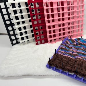 Può includere: Un cappello lavorato a maglia nei toni del marrone, viola e blu è teso su un telaio per maglieria viola. Dietro ci sono tre pannelli per telaio per maglieria in plastica nera, bianca, rossa e rosa.